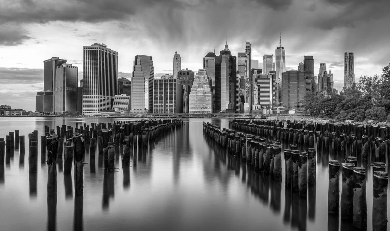 Monochrome foto van de Manhattan skyline met houten palen in het water op de voorgrond – wanddecoratie.